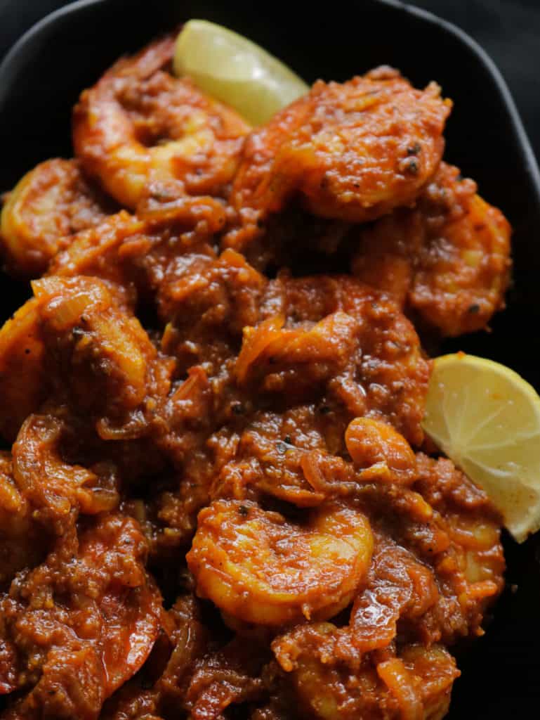  prawn masala placed on a black plate with lime wedges.