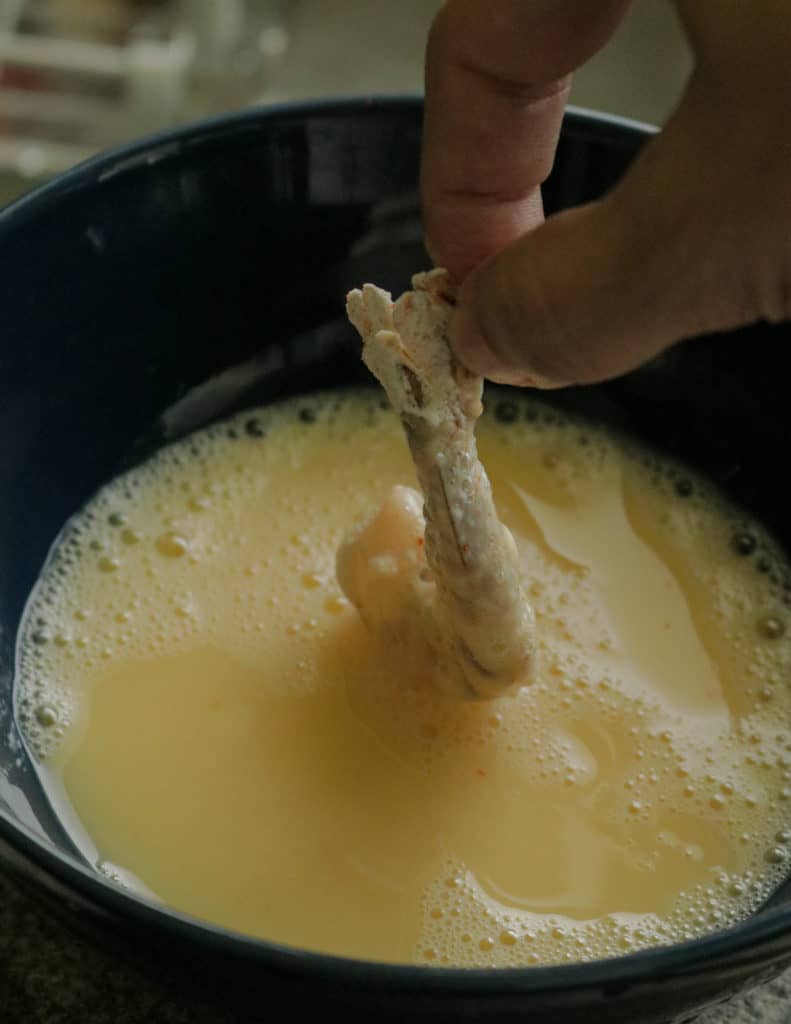 dipping the seasoned and coated flour shrimp into an egg wash to make the breaded shrimp.