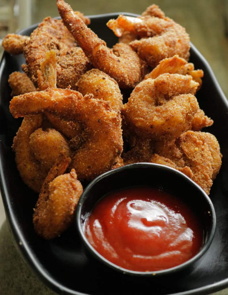 crispy breaded shrimp placed in a black plate served with ketchup/