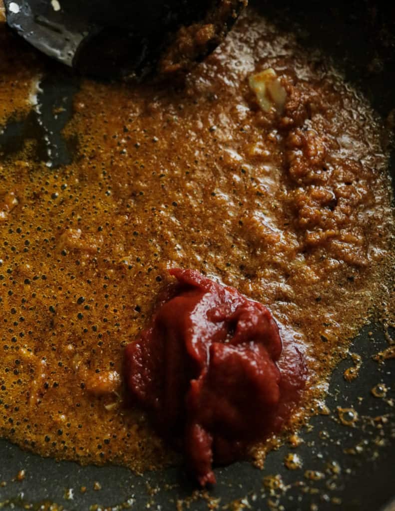 adding the tomato paste to the cooking spice in oil to make the prawn korma.