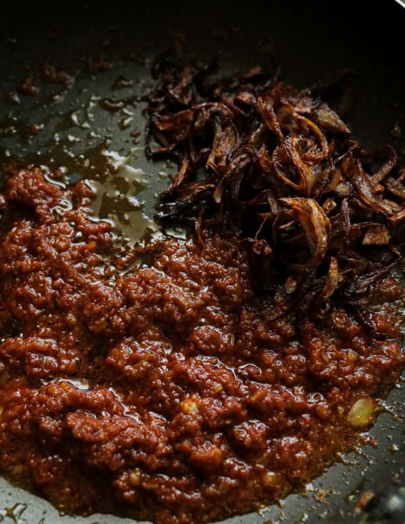 adding the fried onions to the cooked tomato and curry masala to make the prawn korma.