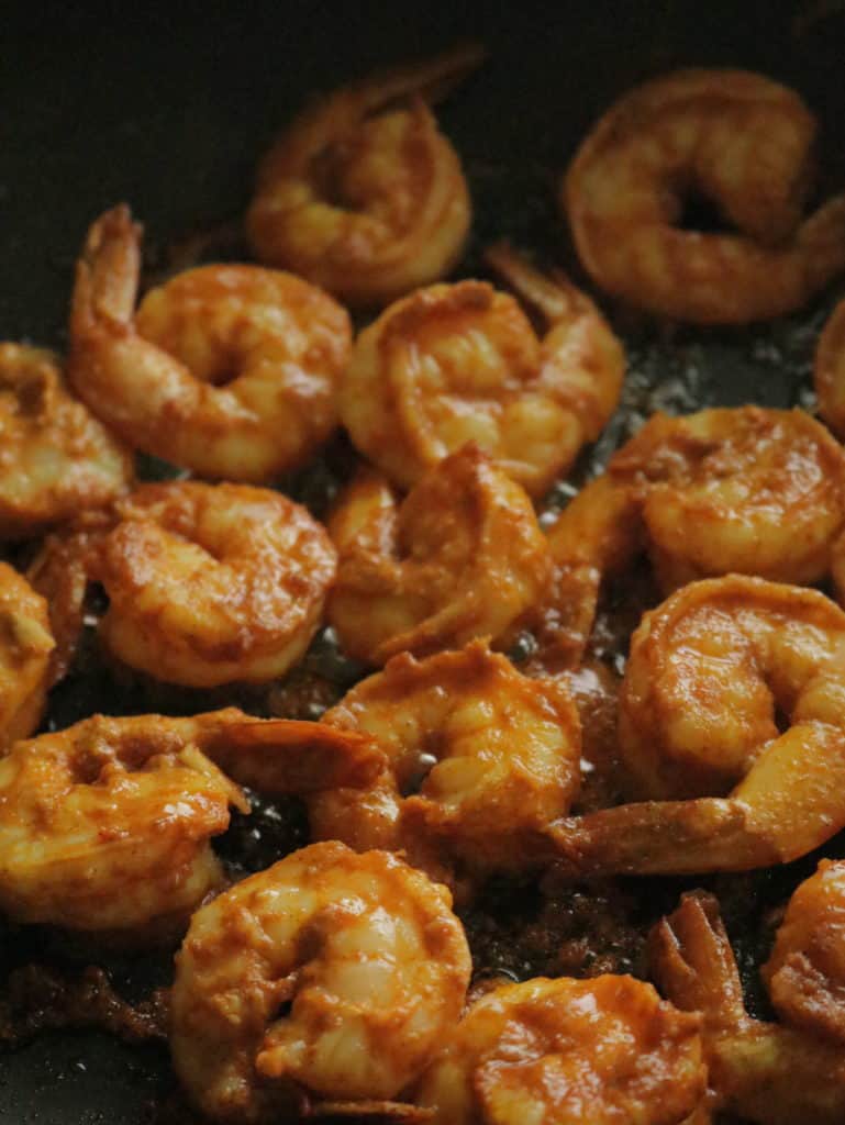 cooking the tandoori marinated shrimp on a stove top.