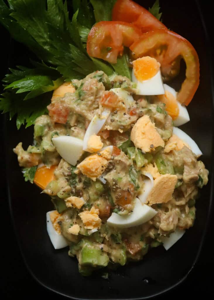 tuna egg salad with celery, tomato , onions and served on a black platter.