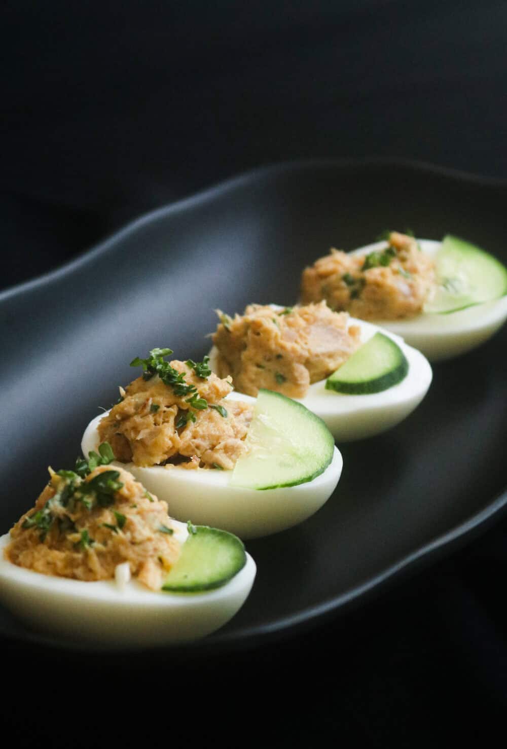 tuna deviled eggs with slices of cucumber and chopped parsley as garnish.