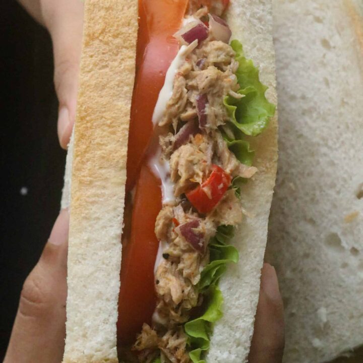 holding a spicy tuna sandwich with a layer of tomato and lettuce.