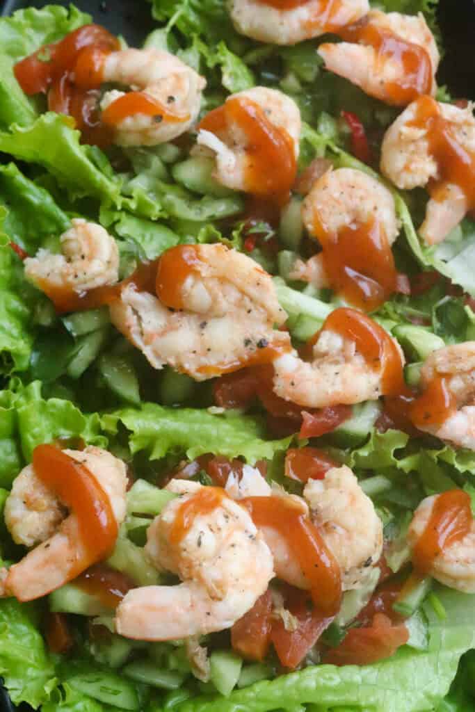 lettuce wraps with shrimp with a layer of chopped cucumber and tomatoes with a drizzle of sauce.