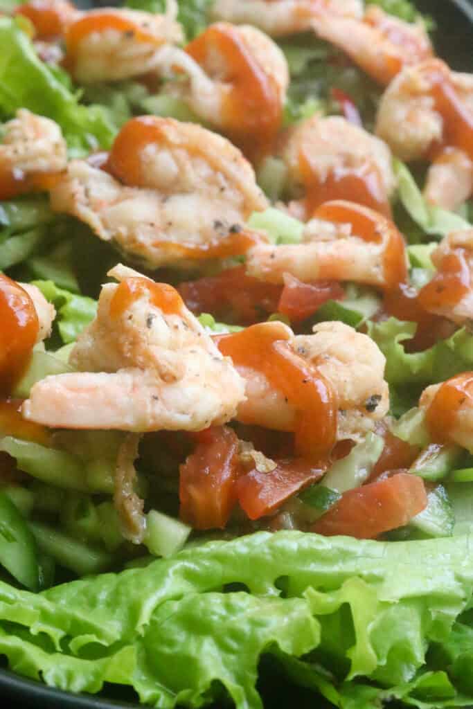 shrimp in lettuce wraps with chopped cucumber, tomatoes and drizzled with sauce.